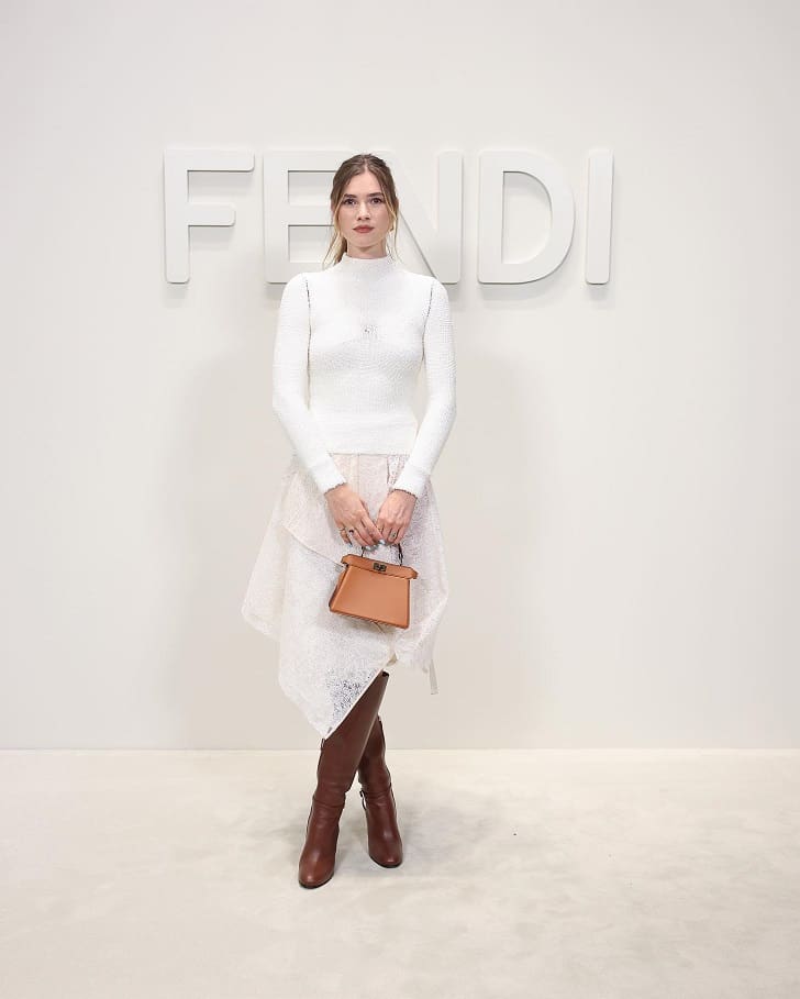 Девушка в асимметричной юбке от Fendi, белом свитере и коричневых сапогах